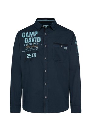Maglietta a maniche lunghe navy con taschino frontale, chiusura a bottone e testo grafico in blu chiaro e arancione. Tessuto di cotone morbido e informale.