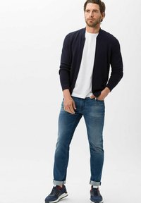 Navy textured cardigan over a white t-shirt, paired with light blue jeans and navy sneakers with red accents. Casual and fitted look.