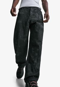 Black denim pants with a faded texture. Designed with a loose fit and straight legs, paired with black lace-up boots.