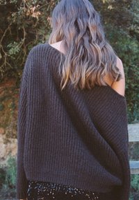 Brun räfflad tröja med off-shoulder-design, bärs över en svart paljetterad kjol. Texturen och den lösa passformen är framträdande egenskaper.