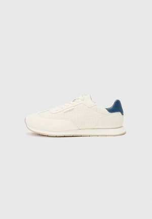 White athletic sneakers with a perforated texture, smooth leather, and a contrasting blue heel accent. Round toe and flat rubber sole.