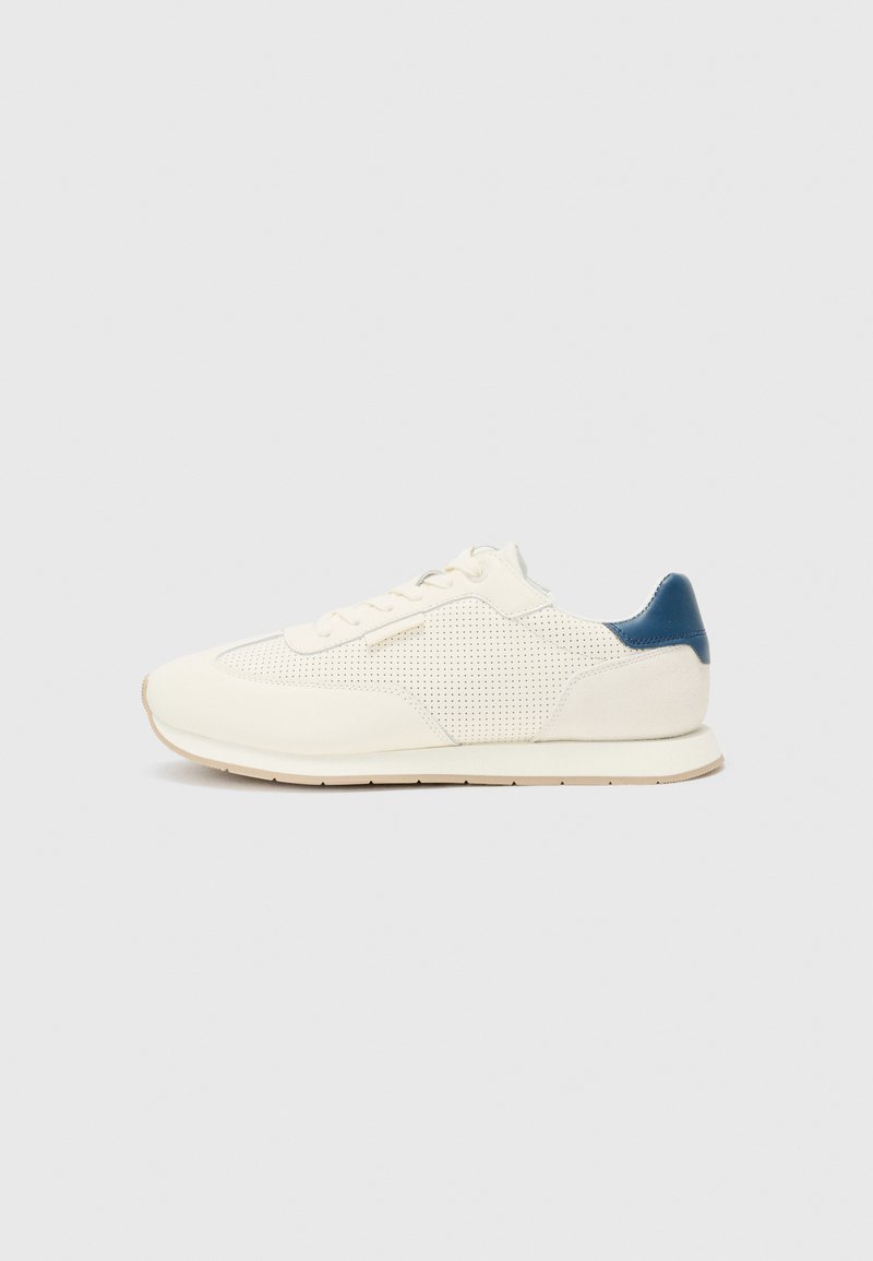 White athletic sneakers with a perforated texture, smooth leather, and a contrasting blue heel accent. Round toe and flat rubber sole.