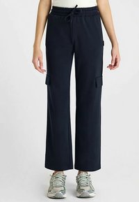 Pantalon cargo bleu marine à coupe décontractée, taille élastique, deux poches latérales et texture lisse, associé à des baskets gris clair.