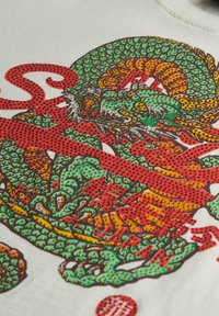 Camiseta blanca con un diseño de dragón colorido en verde, rojo y naranja, con detalles texturizados y acentos gráficos.
