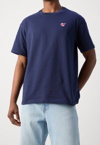 Marineblå bomulds T-shirt med rund hals, korte ærmer og logo detaljer på fronten. Afslappet pasform med en glat tekstur. Sammen med lyseblå jeans.