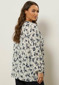 Blumenmuster Langarmbluse in Creme und Marineblau, mit gerafftem Manschettendetail und einem lockeren Schnitt, aus leichtem strukturiertem Stoff gefertigt.