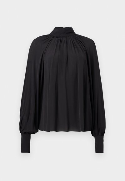 Blouse noire à manches longues avec un col montant, tissu froncé aux épaules et aux poignets, coupe ample au niveau du corps et des manches.