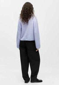 Fioletowy sweter z dzianiny o szerokich rękawach, zestawiony z luźnymi czarnymi spodniami i błyszczącymi czarnymi butami. Miękka faktura i krótki fason.