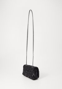 Borsa a spalla nera con paillettes e una lunga tracolla in argento appesa su uno sfondo bianco.