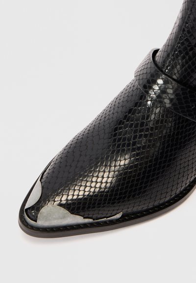 Botine negre cu model de șarpe, cu vârful ascuțit și un finisaj elegant. Au un toc plat și o curea largă în jurul gleznei.