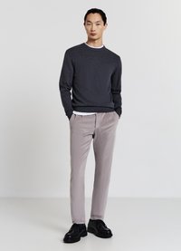 Maglione grigio scuro con texture, camicia bianca a girocollo sotto, pantaloni beige chiaro e scarpe nere. Design semplice e su misura.