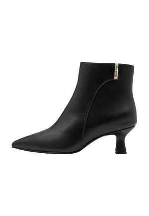 Bottine en cuir noir à bout pointu, talon moyen incurvé et petite étiquette beige près du bord supérieur sur le côté extérieur.