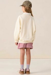 Witte oversized sweatshirt, roze corduroy rok, blauwe sokken met hartpatronen en een panterprint pet. Bruine schoenen met roze accenten.