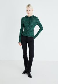 Camisa de cuadros verdes con botones, de manga larga y cuello redondo, combinada con pantalones acampanados negros y botas negras de punta.