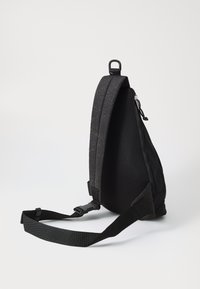 Black shoulder bag with a textured surface, mesh back, adjustable strap, and zipper closure. Features a streamlined, triangular shape.