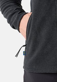 Giacca zip-up grigia scura con texture a coste, dotata di una tasca laterale e di un accento decorativo con la bandiera svedese blu e gialla.