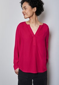 Blusa fucsia de manga larga con escote en V y sutil fruncido en los hombros. Tejido suave con una silueta fluida.