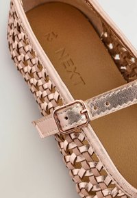 Ballerina in rosé oro intrecciato con cinturino metallico e fibbia regolabile. Presenta una soletta impressa e una texture morbida.