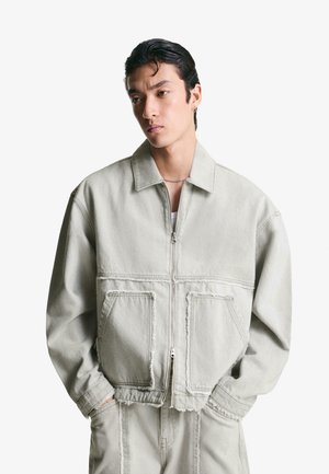 Light gray denim jacket with a zip front, large front pockets, and a relaxed fit. Features frayed seams and a classic collar.