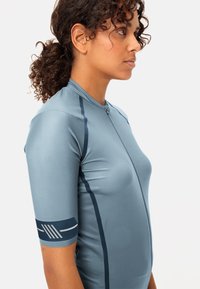 Maillot de cyclisme à manches courtes de couleur bleu clair, fabriqué en tissu extensible. Il comprend une fermeture éclair à l'avant et des accents navy sur les manches avec des lignes de design.