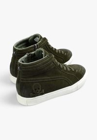 Zapatillas altas de ante verde oscuro con suelas de goma blanca. Presentan un diseño de calavera y huesos cruzados en el lateral y cierre de cremallera en la parte trasera.
