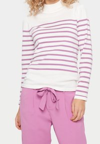 Top de manga larga a rayas en blanco y lavanda con cuello alto, combinado con pantalones rosas que tienen un lazo frontal y una textura suave.