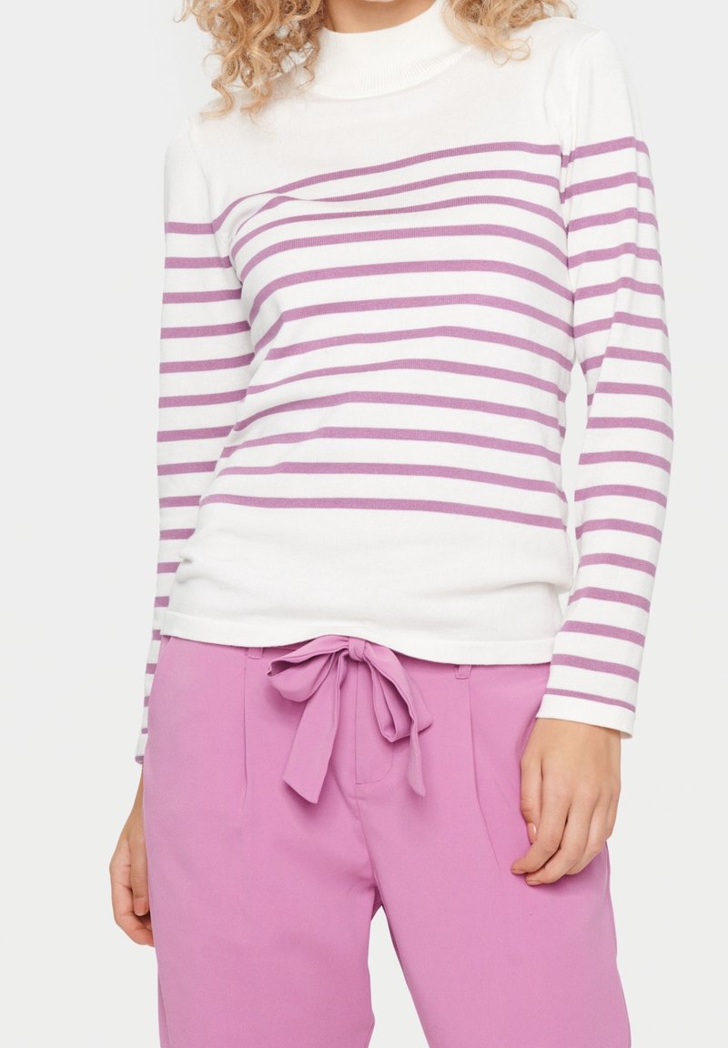 Top de manga larga a rayas en blanco y lavanda con cuello alto, combinado con pantalones rosas que tienen un lazo frontal y una textura suave.
