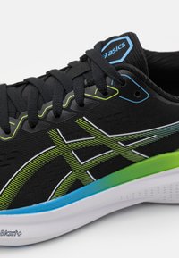 Scarpa sportiva nera con tomaia in rete, dotata di accenti verdi e blu, sovrapposizioni a motivi e una suola bianca imbottita con grip testurizzato.