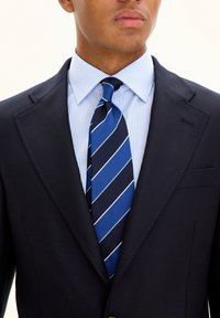 Blazer navy in tessuto testurizzato, camicia dress a righe azzurre chiare e cravatta blu con strisce bianche diagonali. Design aderente con tasche.