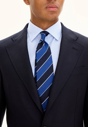 Blazer navy in tessuto testurizzato, camicia dress a righe azzurre chiare e cravatta blu con strisce bianche diagonali. Design aderente con tasche.