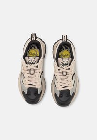 Czarne i beżowe trampki z panelami z siateczki, grubymi gumowymi podeszwami i sznurowadłami. Na języku znajduje się logo, a całość zdobią kontrastowe akcenty.