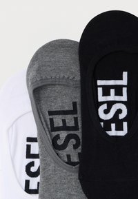 Drei Paar flache Socken in Weiß, Grau und Schwarz mit einer weichen Strickstruktur und dem "DIESEL"-Logo in kontrastierenden Farben.