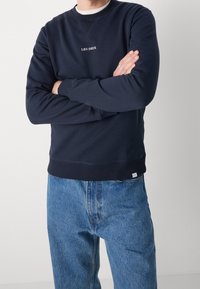 Felpa navy con colletto e polsini a coste. Presenta la scritta "LES DEUX" ricamata in bianco. Abbinata a jeans azzurri chiari. Texture liscia.