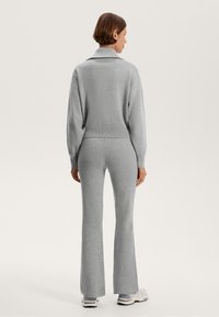 Siva pletena svetilka s ovratnikom in rebrastim robom, v kombinaciji s popolnoma ujemajočimi se širokimi hlačami. Tkanina ima gladko teksturo in sproščen kroj.