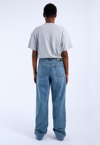 Grijze T-shirt met korte mouwen, gecombineerd met los zittende lichtblauwe denim jeans, met een klassiek vijf-pocket ontwerp en een donker merkembleem.