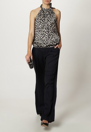 Zwart-wit haltertop met patroon en een geplooide halslijn, gecombineerd met losse zwarte broek en zwarte hoge hakken, een clutch vasthoudend.