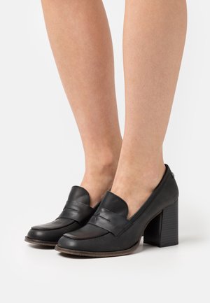 Mocasines de tacón alto de cuero negro con textura suave, punta redonda y detalles de tira ancha. Tacón de bloque resistente, diseño minimalista.