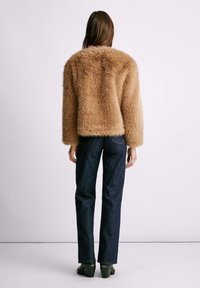 Faux-Fur-Jacke in Beige mit strukturierter Oberfläche, kombiniert mit dunkelblauen Jeans. Die Jacke hat lange Ärmel und ein kurzes Design.