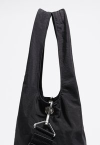 Czarna torba z wyjątkowym podwójnym uchwytem, z metalowym klipsem i teksturowanym paskiem dla pewnego chwytu.