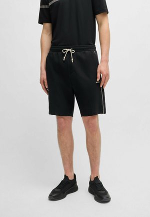Shorts noirs avec une taille élastique et un cordon de serrage, dotés de poches latérales et d'un léger détail rayé, associés à des baskets noires.