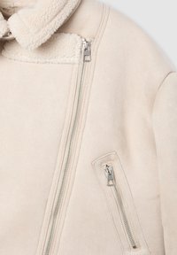 Giacca beige chiaro con colletto in pelliccia, zip argentate e finitura testurizzata. Presenta una tasca frontale con zip e un design con zip laterali.