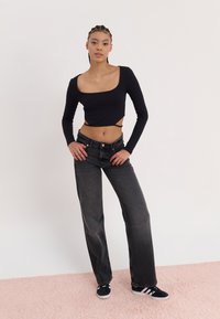 Black long-sleeve crop top, ribbed texture, paired with faded black straight-leg jeans and black sneakers with white stripes.