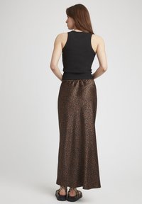 Un débardeur noir côtelé associé à une longue jupe en satin imprimée léopard marron, dotée d'une taille élastique et de sandales plates.