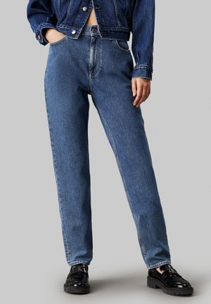 Vaqueros de mezclilla azul de cintura alta con un diseño de pierna recta; tejido texturizado; costuras en contraste; combinados con zapatos de plataforma negros.