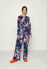 Conjunto de roupa de lounging com padrão floral, apresentando mangas longas e calças largas na cor azul marinho, com detalhes em rosa e verde. Usado com calçado laranja.