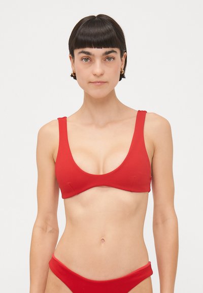 Rotes Bikini-Oberteil mit breiten Trägern, einem tiefen Ausschnitt und einer glatten Textur. Einfaches Design, keine sichtbaren Muster oder Beschläge.