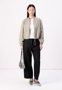 Giacca bomber grigia chiara con polsini elasticizzati, t-shirt bianca con design di farfalla, pantaloni neri a gamba larga e accessori argentati.