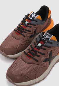 Baskets de sport marron en mesh et daim avec des accents noirs, un talon orange et des lacets multicolores. Comprend une semelle à motif et un logo.