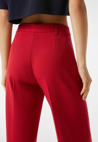 Rode taillepantalons met een gladde textuur, voorzien van een aansluitende tailleband en twee achterzakken. Het ontwerp heeft strakke lijnen en gestructureerde naden.