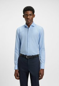 Vaaleansininen, pitkähihaisella paidalla, jossa on hienovarainen ruudullinen kuvio, nappikaulus ja istuva malli, yhdistettynä tummansinisiin housuihin ja vyöhön.